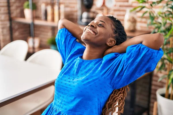 Afro-Amerikalı kadın ellerini başının üstüne koyup evinde sandalyede oturuyor.