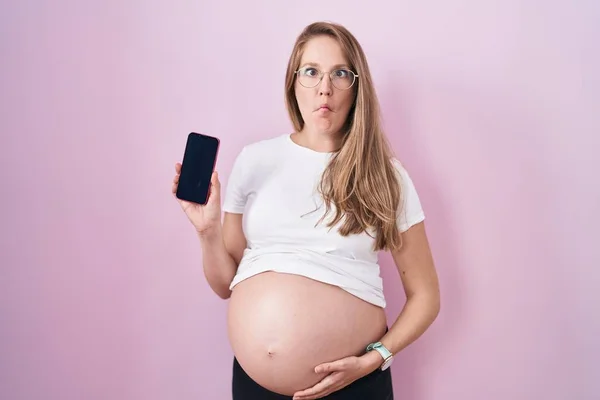 若いです妊娠中の女性ショー腹を保持スマートフォン作り魚顔と口と目を細めて クレイジーとコミカルな — ストック写真