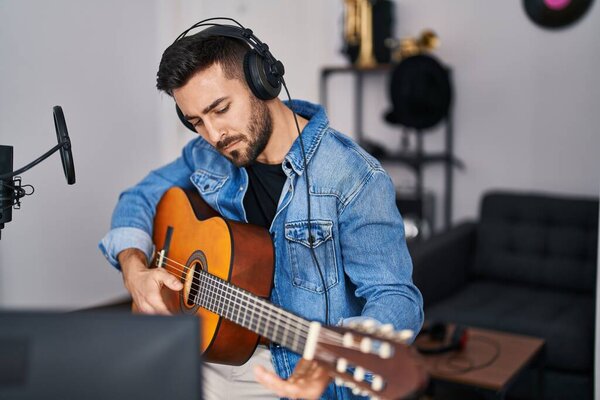 Young hispanic man playing classical guitar at music studio