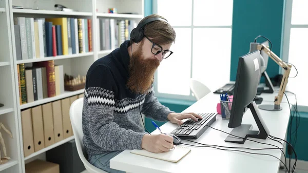 Young Redhead Man Student Using Computer Headphones Writing Notebook Library — Stok fotoğraf