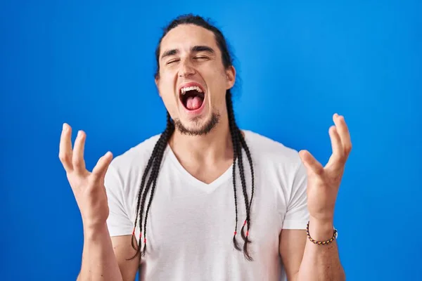 青い背景の上に立って長い髪を持つヒスパニック系の男は 腕を上げ 興奮叫んで目を閉じて成功のために狂気と狂気を祝う 勝者のコンセプト — ストック写真