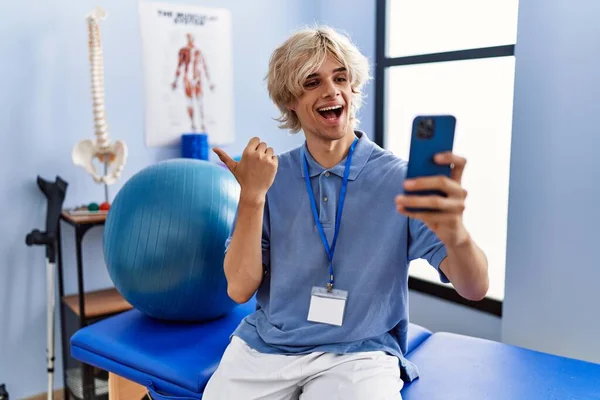 Jovem Trabalhando Clínica Reabilitação Fazendo Videochamada Com Smartphone Apontando Polegar — Fotografia de Stock