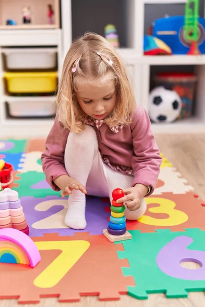 stock image Adorable blonde girl playing with hoops game sitting on floor at kindergarten