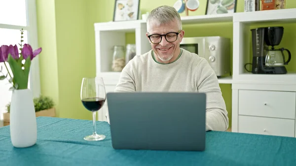 中世の白髪の男自宅でノートパソコンを使用してワインのグラスを飲む — ストック写真