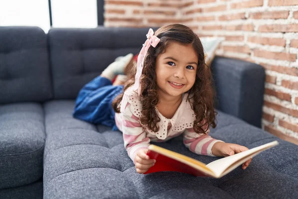 Adorable Hispanic Girl Reading Book Lying Sofa Home — Stockfoto