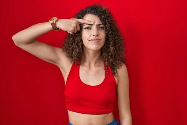 Spaanse Vrouw Met Krullend Haar Rode Achtergrond Wijzend Ongelukkig Pukkelen — Stockfoto