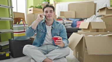 Young hispanic man talking on smartphone drinking coffee at new home