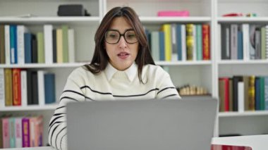 Genç ve güzel İspanyol bir öğrenci kütüphanede dizüstü bilgisayar kullanıyor.