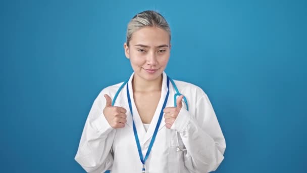 年轻美丽的惊慌失措的女医生用大拇指捂住孤立的蓝色背景 — 图库视频影像