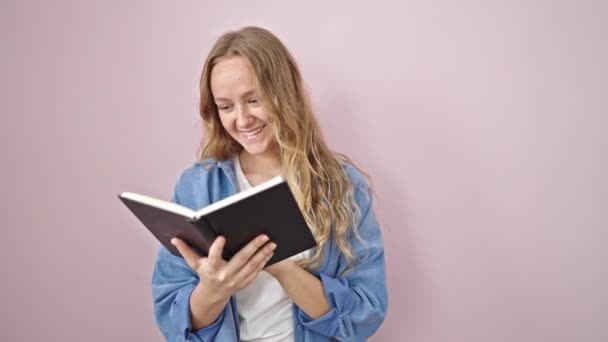 Joven Mujer Rubia Sonriendo Libro Lectura Segura Sobre Fondo Rosa — Vídeo de stock