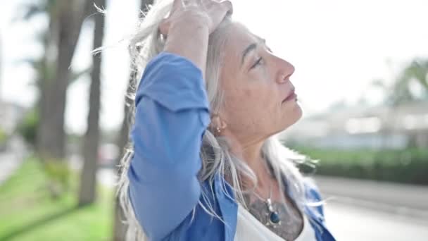 中年白髪の女性が公園で髪を結合真剣な表情で立っています — ストック動画
