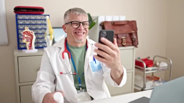 中世の白髪の男性医師は クリニックでオンライン医療相談を受けています — ストック動画