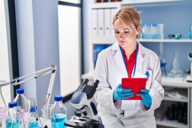 Young blonde woman scientist using touchpad at laboratory