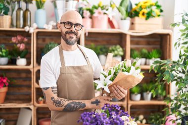 Young bald man florist holding bouquet of flowers at florist