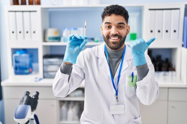 Laboratuvarda çalışan sakallı İspanyol bir adam elinde şırıngayla ağzı açık gülümsüyor. 