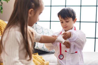 Sevimli kız ve erkek doktor üniforması giyip evde sargı bezi takıyorlar.