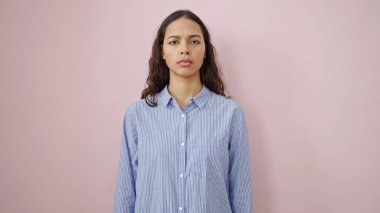 Young beautiful hispanic woman standing with serious expression over isolated pink background
