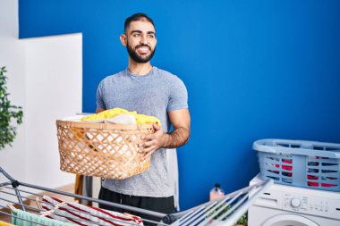 Çamaşır odasında çamaşır sepetini tutan kendine güvenen İspanyol genç adam.