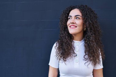 Genç, güzel İspanyol bir kadın, kendinden emin gülümsüyor ve izole edilmiş siyah bir arkaplanda yan tarafa bakıyor.