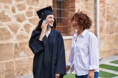 Mezuniyeti kutlayan iki kadın anne ve kız kampüs üniversitesinde akıllı telefondan konuşuyor.