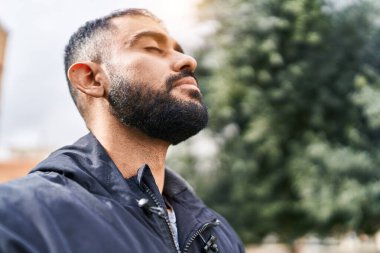 Young hispanic man breathing with closed eyes at park