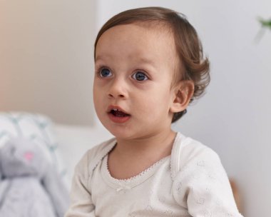 Yatak odasında rahat bir ifadeyle yatakta oturan sevimli İspanyol çocuk.