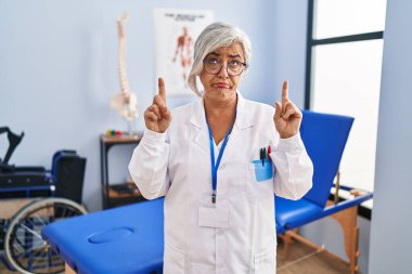 Beyaz saçlı orta yaşlı bir kadın ağrı kesici kliniğinde çalışıyor üzgün ve üzgün görünüyor, parmaklarıyla yön gösteriyor, mutsuz ve depresif.. 