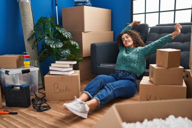 Genç, güzel, İspanyol bir kadın yeni evinde yerde oturmuş kollarını açıyor.