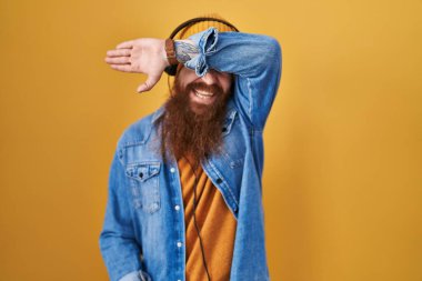 Uzun sakallı, müzik dinleyen, kulaklık takan, gözleri kollarıyla kaplayan neşeli ve komik bir beyaz adam. kör kavram. 