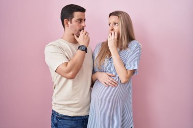 Pembe arka planda bebek bekleyen genç bir çift gergin ve gergin görünüyor. Elleri ağızdan tırnak yiyor. anksiyete. 
