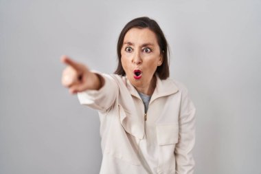 Orta yaşlı İspanyol bir kadın izole edilmiş arka planda dikiliyor. Parmağıyla işaret ediyor. İleride şaşırmış, ağzı açık, şaşırmış bir ifade. 