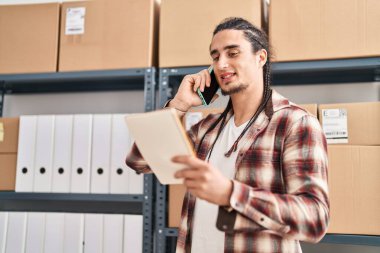 Young man ecommerce business worker talking on the smartphone reading notebook at office