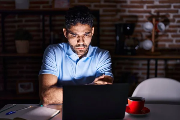 Hispanic man with beard using laptop at night skeptic and nervous, disapproving expression on face with crossed arms. negative person.