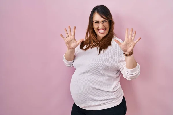 妊娠中の女性立っていますピンクの背景表示と指差しますとともに指番号10ながら笑顔自信と幸せ — ストック写真