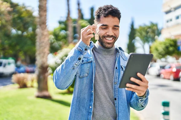 Young hispanic man having video call holding key of new home at park