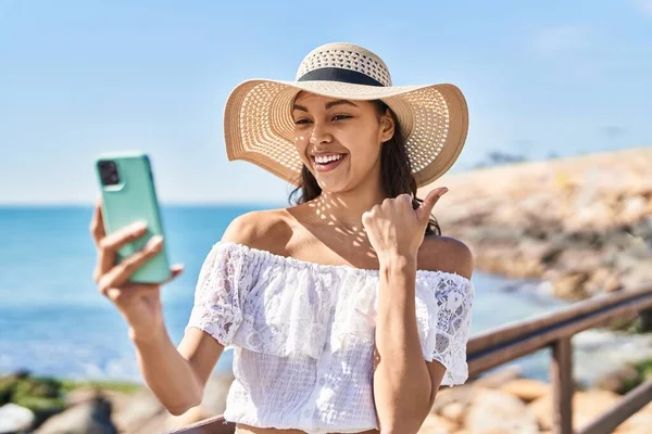 stock image Young brazilian woman taking a selfie photo with smartphone outdoors pointing thumb up to the side smiling happy with open mouth 