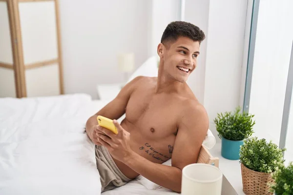 Young Hispanic Man Using Smartphone Sitting Bed Bedroom — Foto Stock