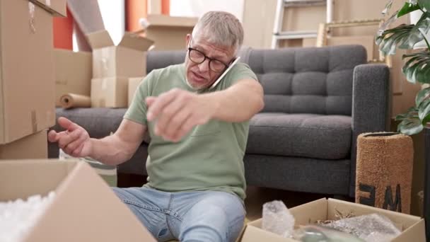 中年白发男人打开包装纸板箱 在新家用智能手机交谈 — 图库视频影像