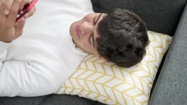 Evdeki kanepede uzanmış akıllı telefon kullanan genç bir İspanyol.