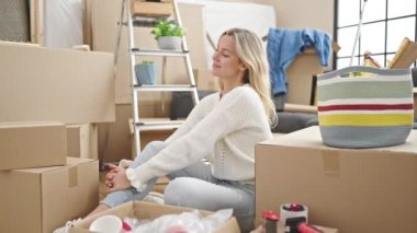 Young blonde woman sitting on floor with winner expression at new home