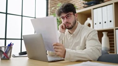 Genç İspanyol iş adamı ofiste dizüstü bilgisayar okuma belgesi kullanıyor.