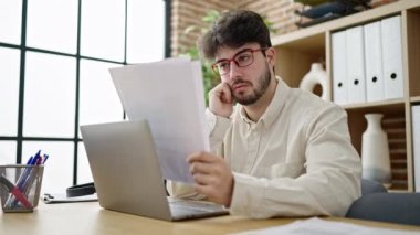 Young hispanic man business worker using laptop reading document at office