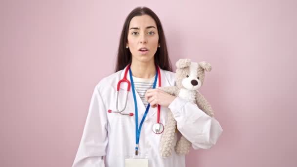 年轻美丽的惊慌失措的女医生抱着泰迪熊 要求安静地对待孤独的粉色背景 — 图库视频影像