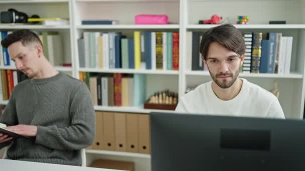 两名使用计算机阅读书籍的男生在图书馆大学学习 — 图库视频影像
