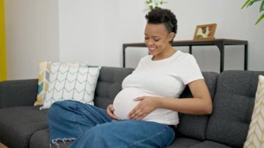 Young pregnant woman touching belly sitting on sofa at home
