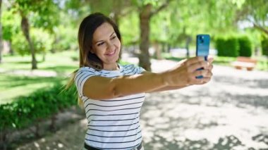 Orta Doğulu bir kadın gülümsüyor. Parkta telefonla özçekim yapıyor.