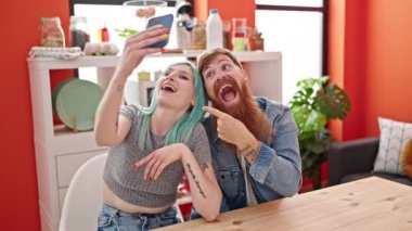 Kadın ve erkek güler yüzlü yemek odasında akıllı telefondan selfie çekerler.