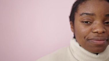 Afro-Amerikalı kadın pembe arka planda kendine güvenen gülümsüyor.