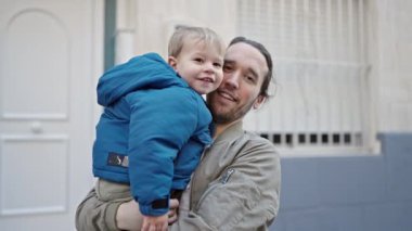Baba oğul gülümsüyor. Kendilerine güveniyorlar. Sokakta sarılıyorlar.
