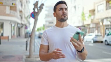 Young hispanic man smiling confident talking on smartphone at street